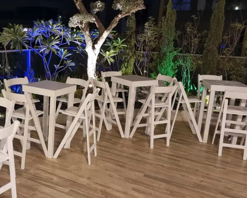 שולחנות בר וכיסאות בר לבנים על במת עץ בתאורת ערב
